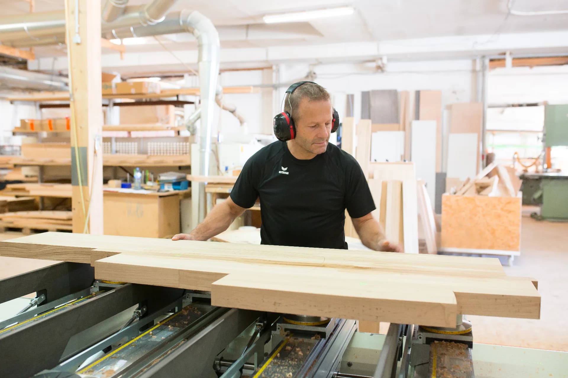 Schreiner mit Gehörschutz an der CNC-Fräse in der Frey-Schreinerei, rohes Eschenholz auf der Maschine