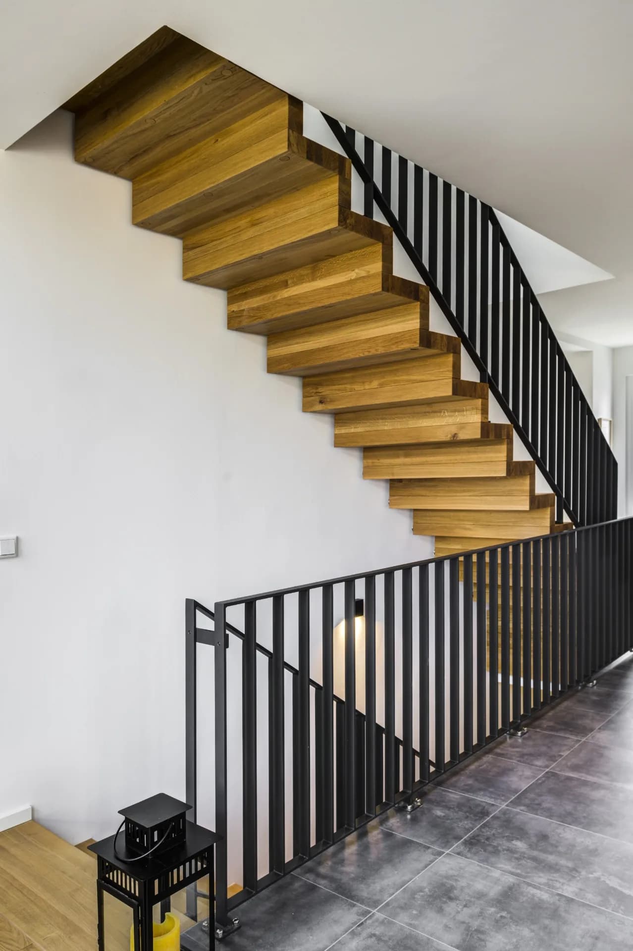 Faltwerktreppe aus massiver Eiche mit schwarzem Stahlstabgeländer über einem Luftraum mit dunklem Fliesenboden