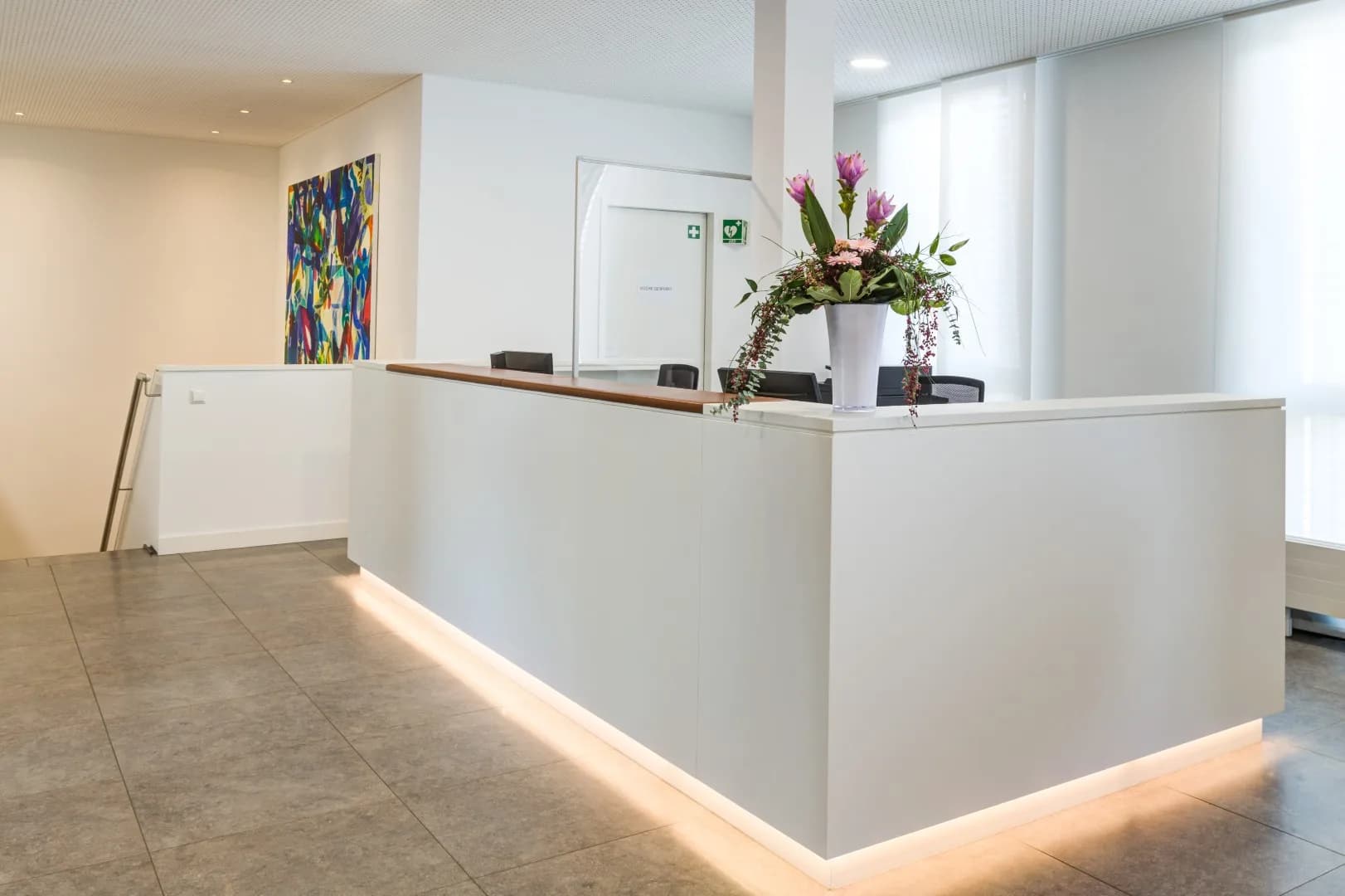 Weiße Empfangstheke mit indirekter Sockelbeleuchtung und Ablage aus Nussbaum in einem hellen Foyer