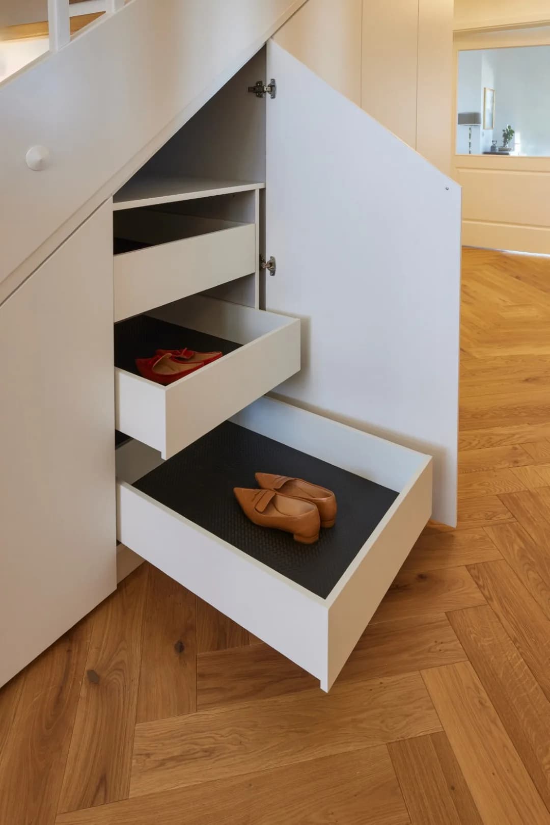 Ausgezogene weiße Schuhauszüge in einem Schrank unter der Treppe, Boden aus Eichen-Fischgrätparkett