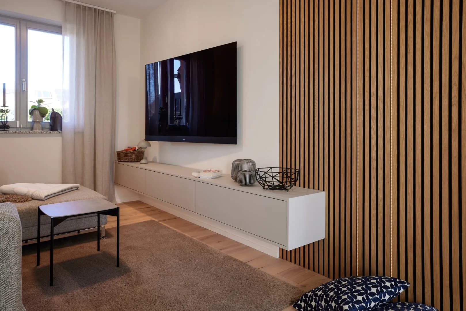 Schwebendes Sideboard in Greige unter dem Fernseher, daneben eine raumhohe Lamellenwand aus Eiche mit indirektem Licht