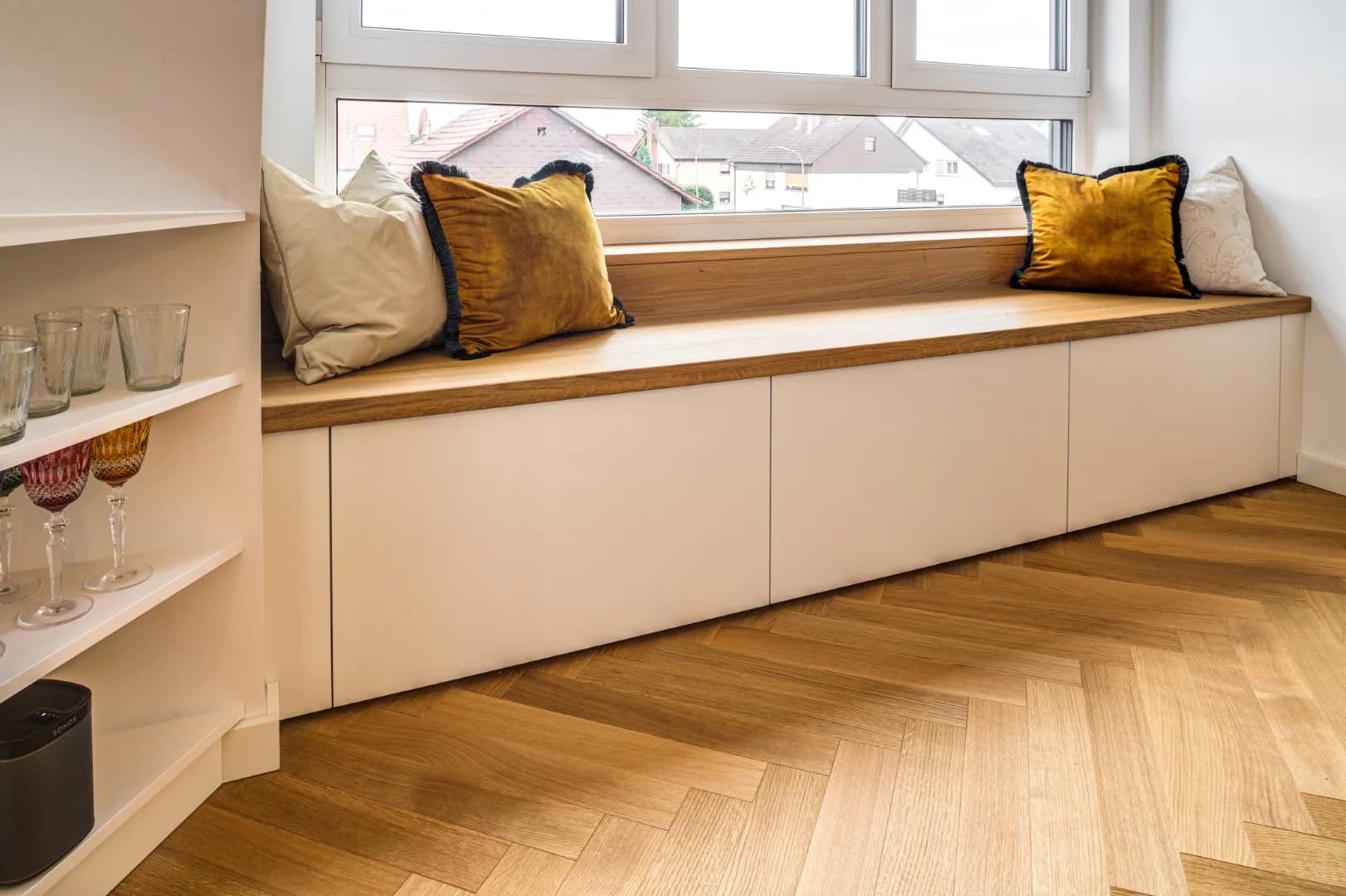 Sitzbank am Fenster mit durchgehender Eichenplatte, weißen Schubkästen darunter und Kissen, Boden aus Eichen-Fischgrätparkett