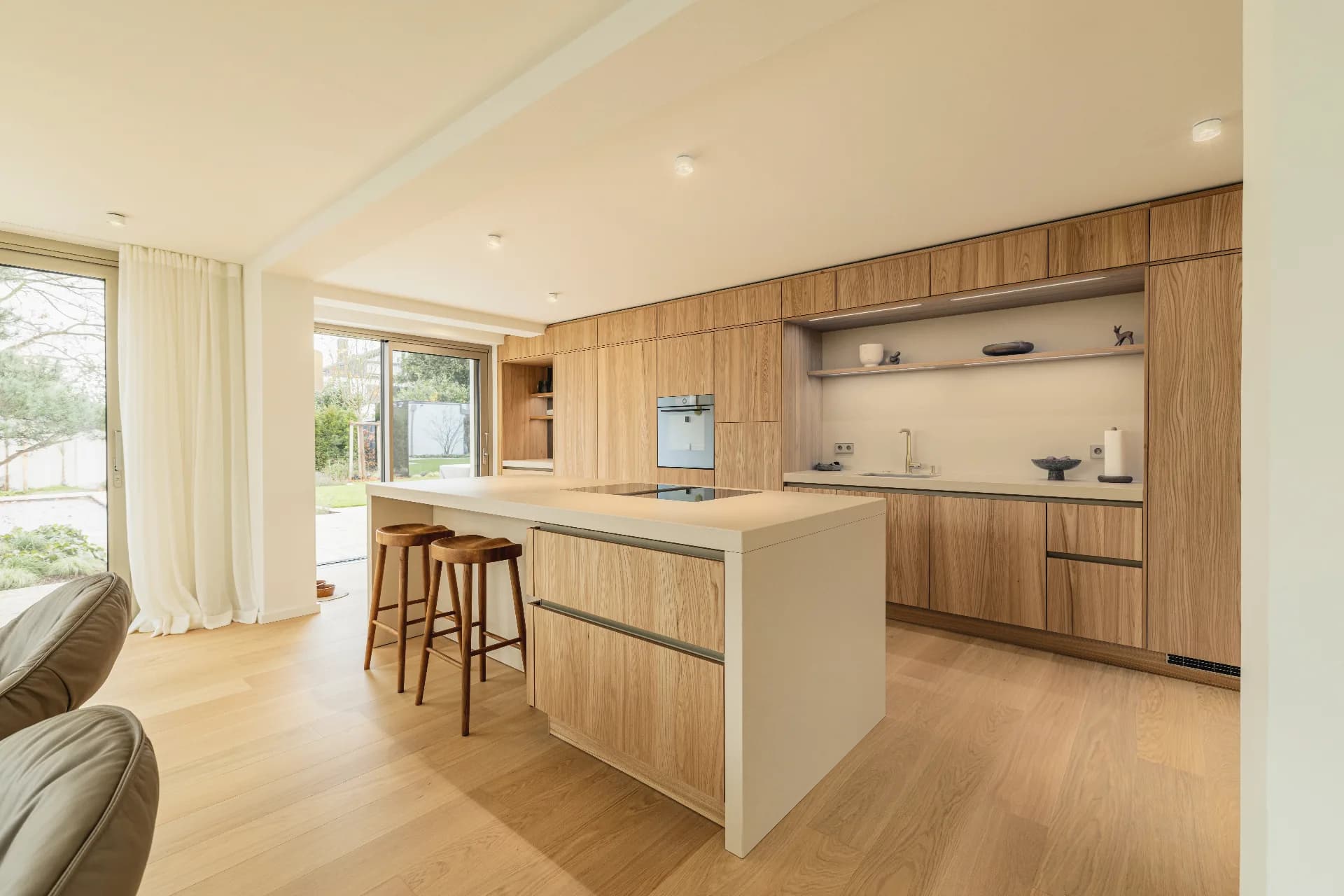 Helle Wohnküche mit cremefarbener Kochinsel, raumhohen Furnierfronten und zwei Barhockern aus Holz