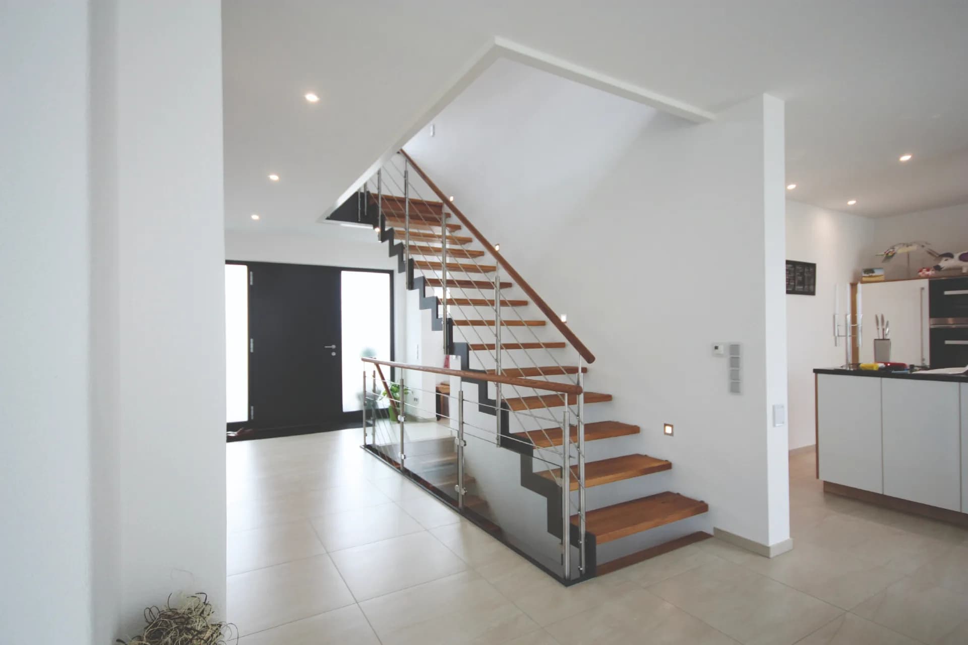 Treppe mit gezackter Stahlwange, Holzstufen und Edelstahlgeländer zwischen Flur und offener Küche